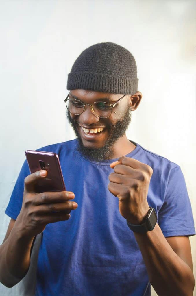 A smiling Hackney business owner looks at his phone and celebrates success. 