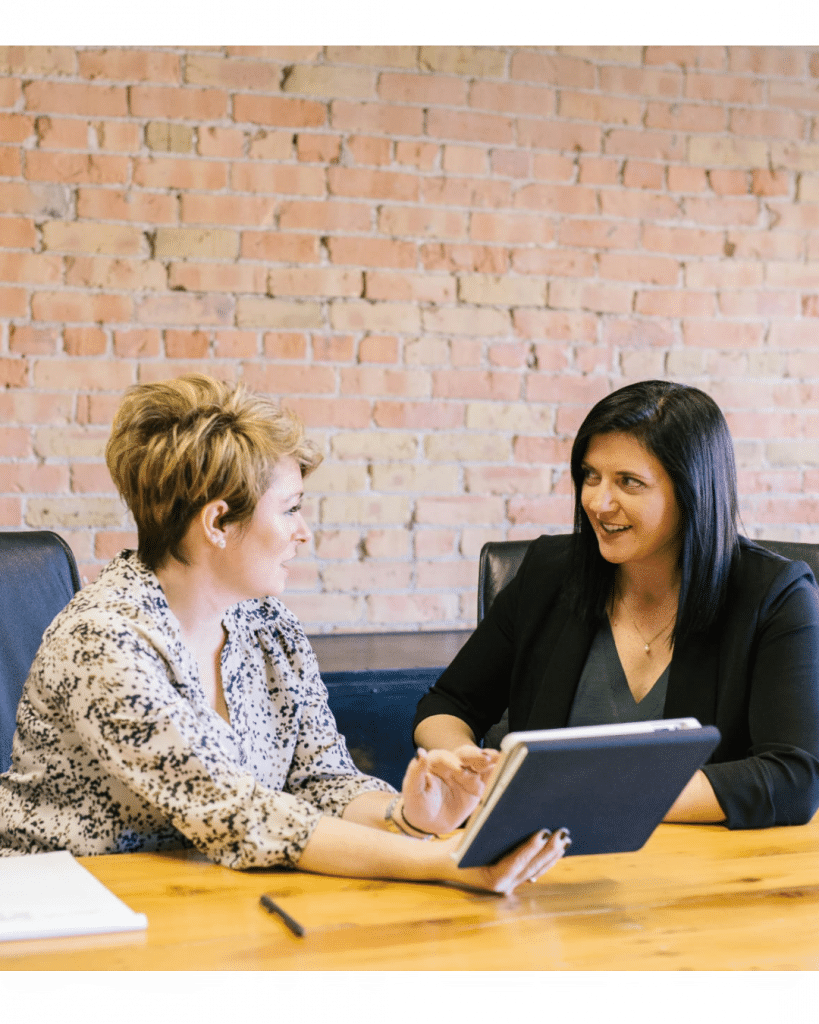 An interviewer sits with a client or member of staff and uses a visual aid to generate conversation. They sit together and look comfortable with healthy eye contact.