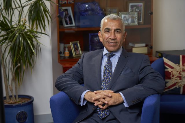 A photo of Karim Fatehi, CEO of the London Chamber of Commerce and Industry. He is late middle-aged with short white hair and is wearing a suit and tie. He sits in a blue armchair, leaning on both armrests and his hands crossed in front of him.